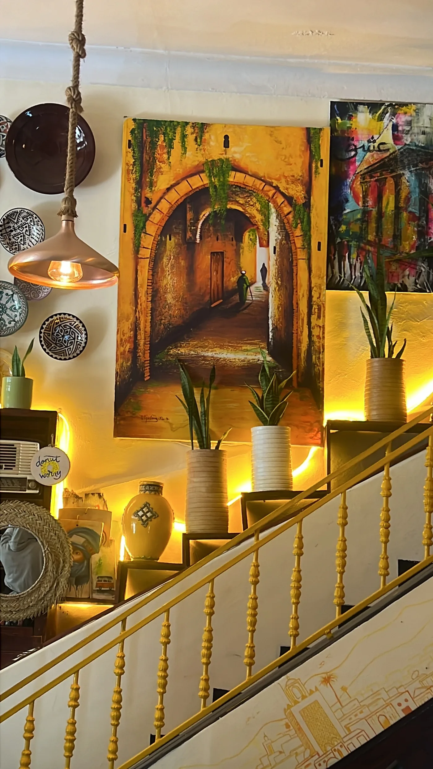 The staircase inside Culture Box with warm yellow light, plants and a street-scene painting
